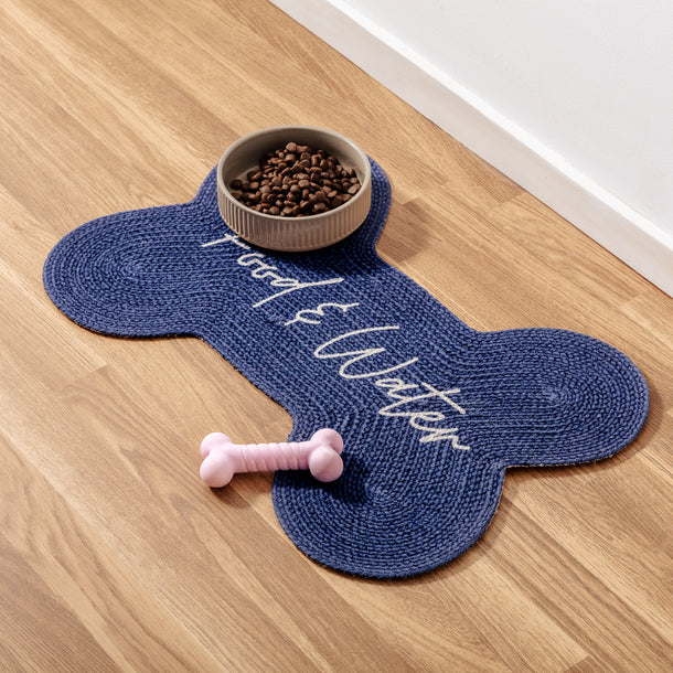 Benedict Pet Placemat on floor with food bowl, bone-shaped design labeled Food and Water, pink dog bone beside it